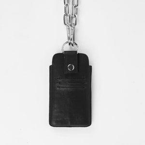 Pu&ograve; includere: Una custodia per telefono in pelle nera con una catena argentata. La custodia ha una patta con chiusura a bottone.