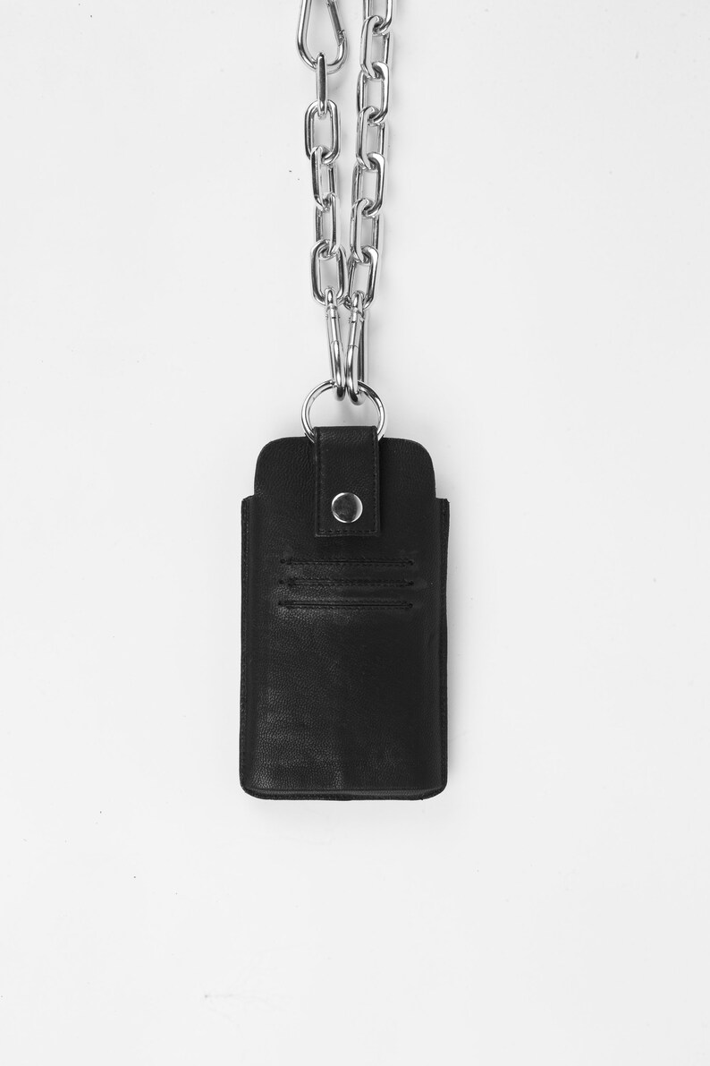 Pu&ograve; includere: Una custodia per telefono in pelle nera con una catena argentata. La custodia ha una patta con chiusura a bottone.