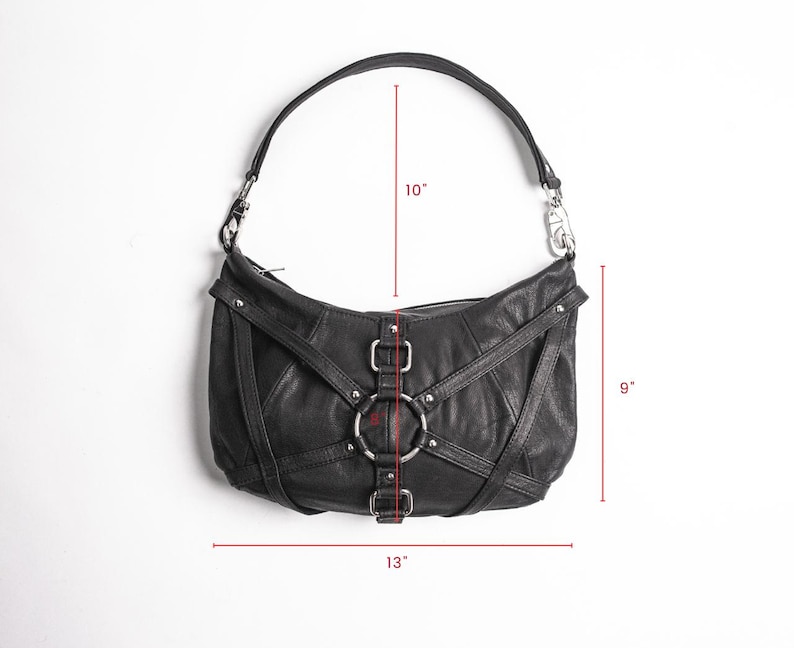 K&ouml;nnte beinhalten: Schwarze Schultertasche aus Leder mit geschwungener Form. Die Tasche hat silberfarbene Hardware, einschlie&szlig;lich Ringe und Schnallen. Der Riemen misst 25 cm, die H&ouml;he betr&auml;gt 23 cm und die Breite 33 cm.