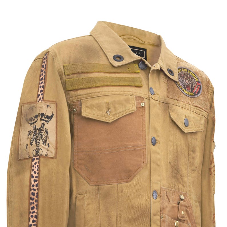 Puede incluir: Chaqueta vaquera color canela con m&uacute;ltiples parches y adornos. Presenta un gr&aacute;fico de esqueleto, detalles de estampado de leopardo y un parche que dice "Flying Tigers". Incluye m&uacute;ltiples bolsillos y cierres de bot&oacute;n.