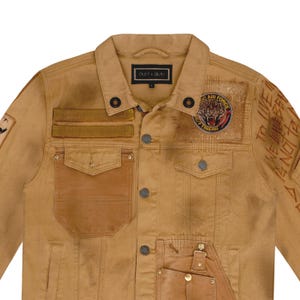 Puede incluir: Chaqueta vaquera color canela con m&uacute;ltiples bolsillos, parches y detalles desgastados. Cuenta con una etiqueta "DUST + BEAU" y un parche con un tigre y las palabras "Air Force Tiger". La chaqueta tiene cierres de bot&oacute;n y costuras decorativas.