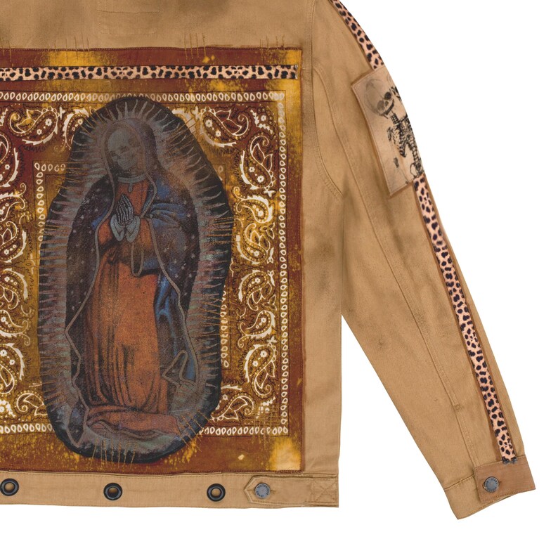 Puede incluir: Chaqueta vaquera color canela con una imagen impresa de la Virgen Mar&iacute;a en la espalda. La chaqueta tiene un borde con estampado de cachemira, detalles de manga con estampado de leopardo y un peque&ntilde;o parche con un dise&ntilde;o de esqueleto. La chaqueta tiene cierres de bot&oacute;n.