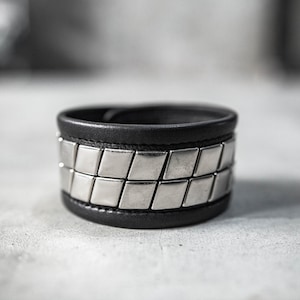 May include: A black leather bracelet with a silver metal band of square-shaped studs.