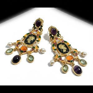 May include: Elaborate gold earrings featuring a black cameo design, complemented by purple, orange, and green gemstones, and faux pearl drops. These earrings have a vintage, regal style.
