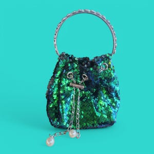 Puede incluir: Un pequeño bolso de mano verde y azul con lentejuelas, una cadena plateada y un asa de anillo plateada.