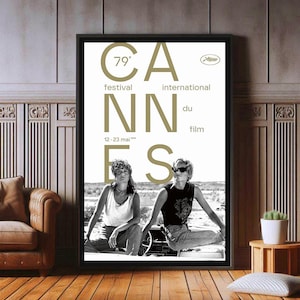 Puede incluir: Póster enmarcado en blanco y negro para el 79º Festival Internacional de Cine de Cannes. El póster presenta la palabra "Cannes" en letras grandes, con las fechas del festival y dos personas sentadas en un coche.