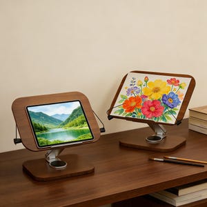 May include: Two wooden tablet stands with adjustable angles. One displays a landscape image, the other a floral watercolor painting. Both stands have a dark wood finish and silver-colored adjustable arms.