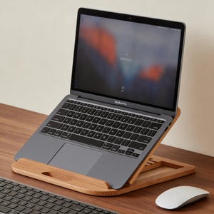 Könnte beinhalten: Ein graues MacBook Pro Laptop steht auf einem Laptop-Ständer aus Holz. Der Laptop-Bildschirm ist geöffnet und zeigt ein verschwommenes Bild. Eine weiße Maus und eine schwarze Tastatur befinden sich ebenfalls auf dem Holztisch. Der Ständer hat eine natürliche Holzoberfläche.