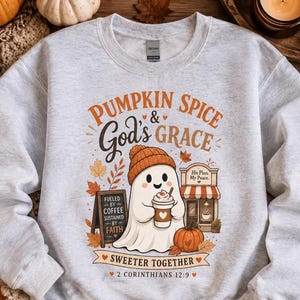 Könnte beinhalten: Ein hellgraues Sweatshirt mit Rundhalsausschnitt und einer Grafik eines Geistes mit orangefarbener Mütze, der einen Kaffeebecher hält. Der Text lautet PUMPKIN SPICE & GOD'S GRACE, FUELED BY COFFEE SUSTAINED BY FAITH, SWEETER TOGETHER und 2 CORINTHIANS 12:9.