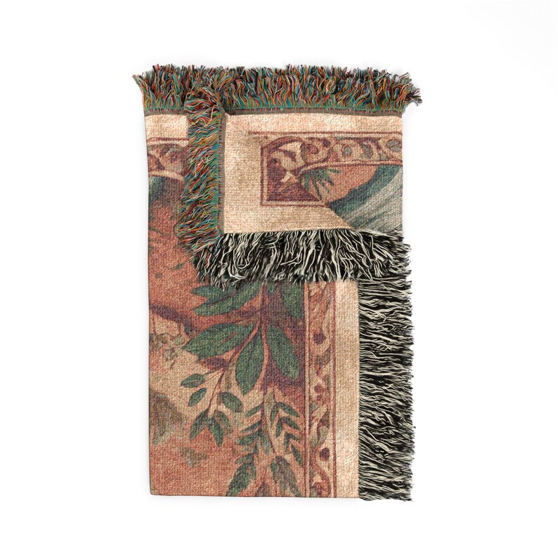 May include: A woven throw blanket featuring a folded corner that reveals a multi-colored design with green leaves, brown tones, and decorative borders. The edges of the blanket are finished with a textured, multi-colored fringe trim.