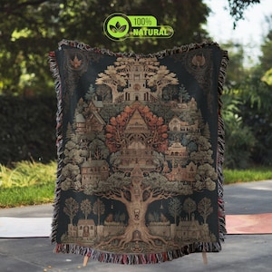 May include: A woven tapestry blanket featuring a detailed illustration of a tree with a village built into its branches. The blanket has a dark teal background and a fringed edge. The text "100% NATURAL" is in the upper right corner.