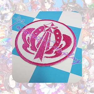 May include: A circular embroidered patch with a white background and a pink design. The design features a star, a horseshoe shape, and a ribbon. The patch is set against a blue and white checkered background, with anime-style characters in the background.