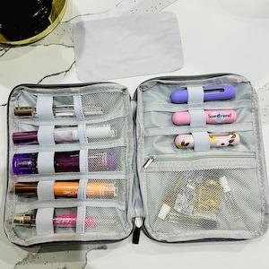 May include: A gray, zippered travel case, open to reveal multiple perfume bottles and accessories. The case has mesh pockets and elastic straps to secure the contents. Some bottles are visible, along with a pink tube with the text "ScentFriend".