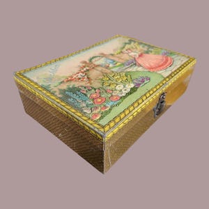 Peut inclure: Boîte rectangulaire vintage avec un extérieur marron tissé et un couvercle à charnière. Le couvercle présente une illustration colorée d'une femme en robe rose dans une scène de jardin. La boîte est bordée de jaune et a un fermoir en métal.