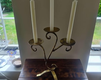 Può includere: Un candelabro in metallo dorato con tre portacandele e un design decorativo a scorrimento. Tre candele bianche sono posizionate nei portacandele.
