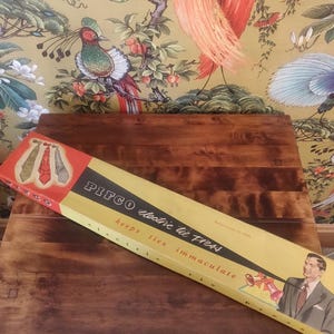 Può includere: Una scatola gialla e rossa con il testo "PIFCO electric tie press" e "keeps ties immaculate". La scatola mostra un uomo in abito e cravatta, e un primo piano di un ferro da stiro per cravatte.