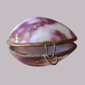 May include: A clam shell-shaped trinket box with a marbled purple and white design. It has a bronze-coloured metal trim and hinge. The box is open, revealing the interior. The design resembles a natural shell.