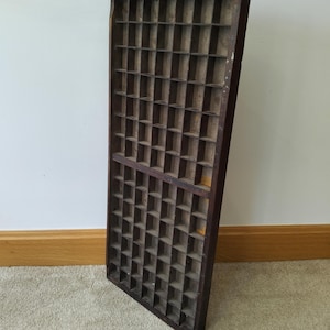 May include: A rectangular dark brown wooden printer's tray featuring a grid of numerous small, square compartments. The vintage storage organiser has a weathered finish with visible wood grain and a sturdy frame, designed for sorting small items.