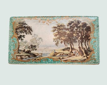 May include: A rectangular tray with a teal and gold border. The tray features a painted scene of a landscape with trees, a river, and a bridge.
