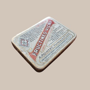 May include: Vintage tin of Fructines-Vichy, a French medicinal product. The tin is rectangular with rounded corners, featuring red and white text on a silver background. The text includes the product name and various health conditions.
