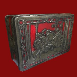May include: A rectangular metal box featuring a raised silver-toned relief of figures on horseback riding through a forest. The design is set against a vibrant red background, framed by an intricate silver-toned border with geometric patterns.
