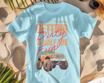 Peut inclure: Un t-shirt bleu clair avec un motif de monster truck et le texte "Getting Dirty is Half the Fun".