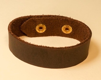 May include: A brown leather bracelet with two gold metal snaps.