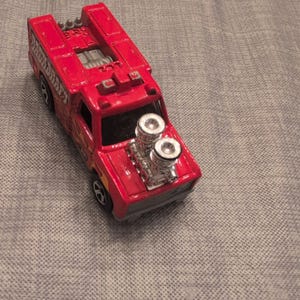 Può includere: Un camion giocattolo rosso con dettagli del motore argentati e ruote nere. Il camion ha un design a pianale e un motore dettagliato. Il camion giocattolo è un classico da collezione.
