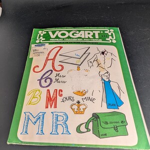 May include: A Vogart 122 repeat transfer pattern sheet with a green border. The sheet features various line art designs including letters A, B, C, M, R, crowns, the text His, Hers, Yours, Mine, a person wearing a scarf, and a school bag with the word School.