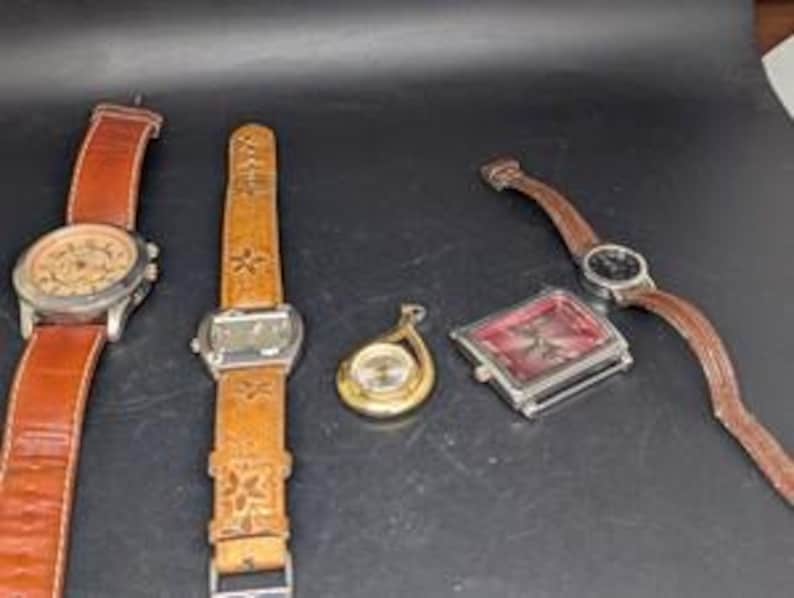 May include: Five watches with leather bands and various face designs. The watches include a round silver watch with a brown leather band, a rectangular watch with a floral embossed leather band, a gold pendant watch, and a square watch with a red face.