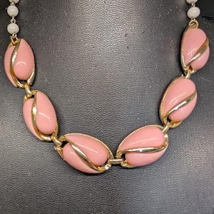 May include: A vintage necklace with pink, teardrop-shaped links, gold-tone accents, and small white beads. The necklace is connected by gold-tone links. The jewellery is displayed against a dark background. The necklace is a classic piece of costume jewellery.