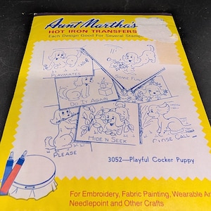 May include: A yellow and white Aunt Martha's Hot Iron Transfers packet featuring blue line art illustrations of cocker spaniel puppies. The text includes 'Playmates', 'Some Fun', 'Do It Again', 'Hide 'n Seek', 'Close Call', 'Please', and '3052-Playful Cocker Puppy'.