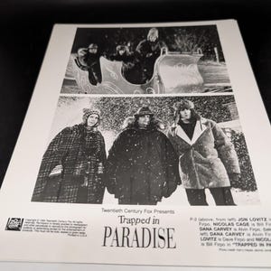 May include: Black and white promotional image for the film "Trapped in Paradise." The image is divided into two sections, with scenes of people in winter clothing. The film's title is prominently displayed.