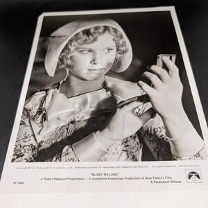 Può includere: Fotografia in bianco e nero di una giovane persona con cappello e abito fantasia, che tiene in mano un piccolo oggetto. L'immagine è un fotogramma promozionale del film "Bugsy Malone", una presentazione di Robert Stigwood e un'uscita Paramount.