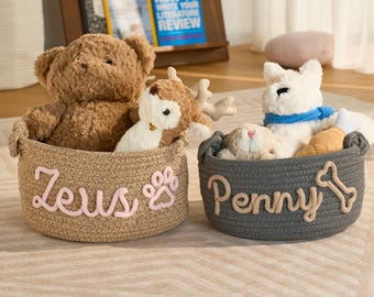 May include: Two woven rope baskets, one tan and one gray, each filled with plush toys. The tan basket has the name "Zeus" and a paw print, while the gray basket has "Penny" and a bone. The baskets sit on a patterned rug.