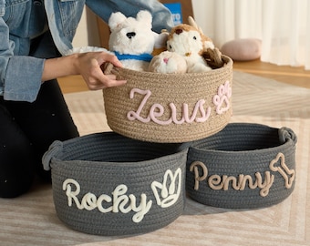 May include: Three gray and beige rope storage baskets with personalized names: "Zeus", "Rocky", and "Penny". The baskets are filled with stuffed animal toys.