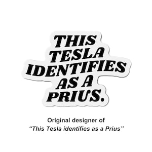 May include: A white sticker with the text "THIS TESLA IDENTIFIES AS A PRIUS" in bold black letters. Below the text is the phrase "Original designer of 'This Tesla identifies as a Prius'".