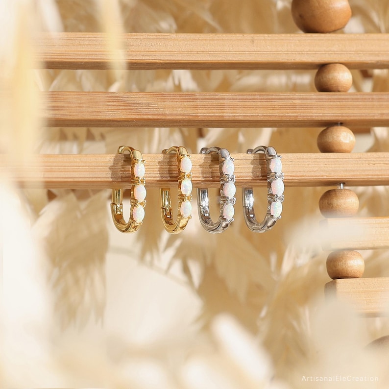 May include: Four hoop earrings arranged in a row, featuring two gold-toned hoops and two silver-toned hoops. Each earring is set with three small, oval-shaped white opalescent stones along the front curve of the circular metal band.