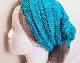May include: A teal blue knitted headband with a textured pattern. The headband is worn on a mannequin with long brown hair.