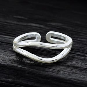 May include: A silver ring with a simple, modern design. The ring is made of two thin bands that intersect in the middle, creating a unique and stylish look.