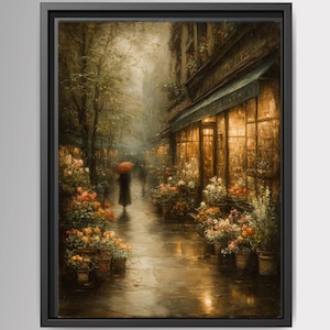 May include: A framed wall art print depicting a rainy city street scene at dusk. A figure holding a bright red umbrella walks along a wet sidewalk lined with glowing storefront windows and numerous potted flower arrangements in warm tones.