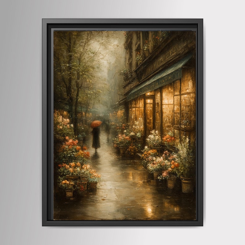 May include: A framed wall art print depicting a rainy city street scene at dusk. A figure holding a bright red umbrella walks along a wet sidewalk lined with glowing storefront windows and numerous potted flower arrangements in warm tones.