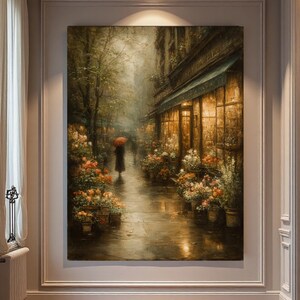 May include: A large rectangular wall art print depicting a rainy city street scene at dusk. A figure with a bright red umbrella walks along a wet sidewalk lined with potted flowers and a glowing storefront window with warm golden interior lighting.