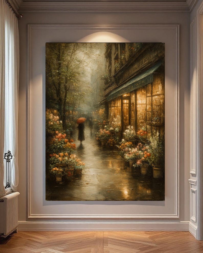 May include: A large rectangular wall art print depicting a rainy city street scene at dusk. A figure with a bright red umbrella walks along a wet sidewalk lined with potted flowers and a glowing storefront window with warm golden interior lighting.