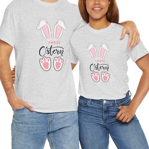 May include: Two gray t-shirts with a pink bunny rabbit design and the text "Frohe Ostern" on them. The shirts are being modeled by two people.
