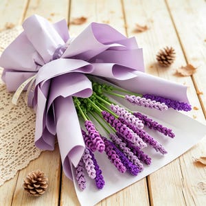 Könnte beinhalten: Ein Strauß aus gehäkelten Lavendelblüten in verschiedenen Lila- und Grüntönen, eingewickelt in hellviolettes Papier. Die Stiele sind grün und die Blütenköpfe sind mit Garnschlingen texturiert, was ein realistisches Blumenarrangement ergibt.