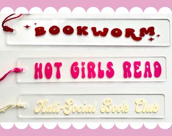 Peut inclure: Trois marque-pages en acrylique transparent avec des dictons différents. Le marque-page du haut a le texte "BOOKWORM" en rouge. Le marque-page du milieu a le texte "HOT GIRLS READ" en rose. Le marque-page du bas a le texte "Anti-Social Book Club" en crème.