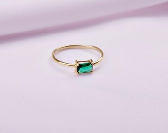 Op de afbeelding: Een gouden ring met een rechthoekige groene edelsteen.
