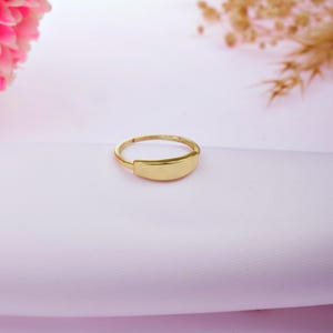 Op de afbeelding: Een eenvoudige gouden ring met een platte, rechthoekige bovenkant. De ring ligt op een witte achtergrond.