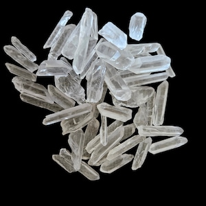 May include: A pile of clear quartz crystal points, also known as rock crystals, on a black background. The crystals are various sizes and shapes, with some being long and thin, while others are shorter and thicker.